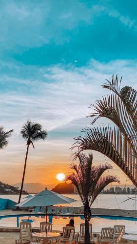 a beach with chairs and a palm tree and the sunset at Ilha Porchat Hotel in São Vicente