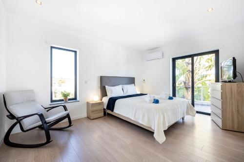 a white bedroom with a bed and a chair at Villa Celestine in Portimão