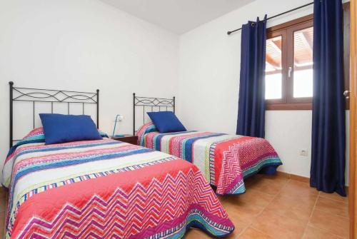 プラヤ・ブランカにあるVilla del Surのベッドルーム1室(カラフルなシーツと窓付きのベッド2台付)