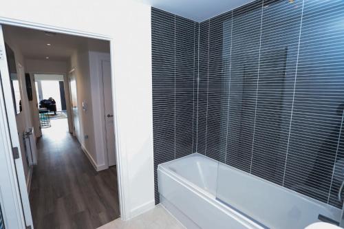 a bathroom with a tub and a tile wall at LOVELY 2 BED APARTMENT WITH PARKING in Woolwich