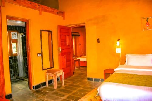 a bedroom with orange walls and a bed and a bathroom at Prakriti Aalay - Riverside Mountain View Boutique Eco Resort in Dharamshala