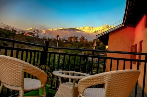 two chairs and a table on a balcony with mountains at Prakriti Aalay - Riverside Mountain View Boutique Eco Resort in Dharamshala