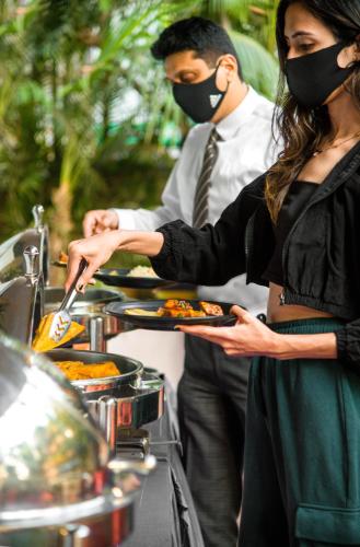 a man and woman wearing masks holding plates of food at Hotel Oriental Aster - Mumbai International Airport in Mumbai