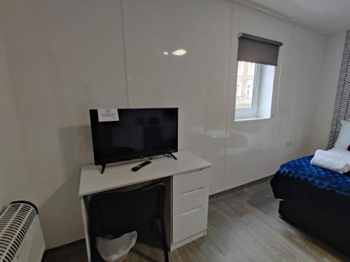 a living room with a tv on a desk with a bed at Double Ensuite Rooms in Swansea