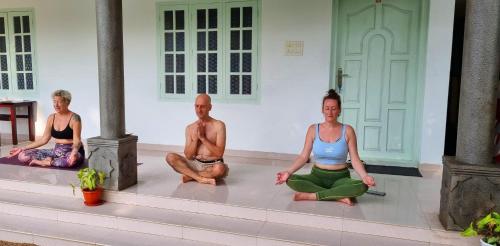 um grupo de três pessoas sentadas numa pose de yoga em Chilanka Lake view Resort em Alappuzha