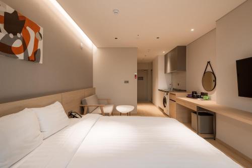 a hotel room with a white bed and a kitchen at Chestertons Sokcho in Sokcho