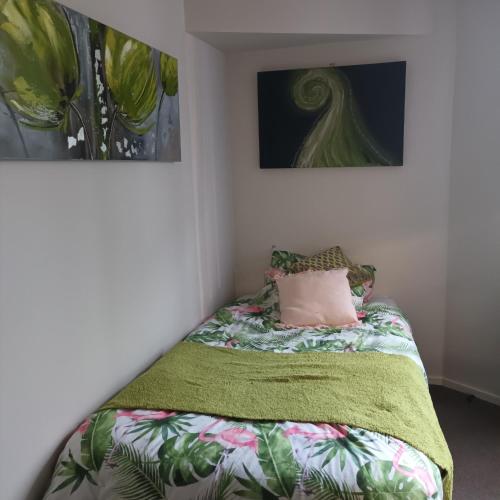 a bed with a green blanket and a pink pillow at Tiwai Waka Retreat in Wellington