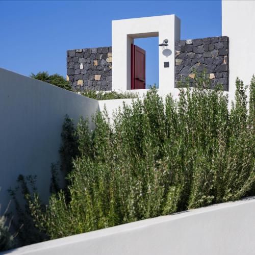 a fence with plants in front of a house at Potnia Theron Suites in Akrotiri