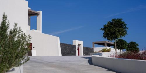 a white house with a driveway and a tree at Potnia Theron Suites in Akrotiri
