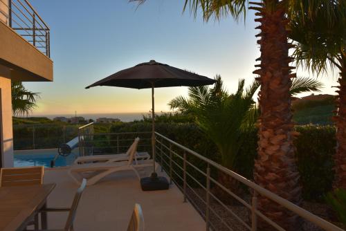 a patio with an umbrella and a chair and a table at Exclusieve Villa met zeezicht en privézwembad in Atalaia in Lourinhã