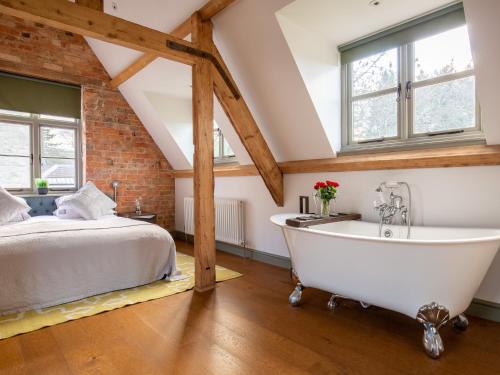 Schlafzimmer im Dachgeschoss mit einem Bett und einer Badewanne in der Unterkunft The Hayloft in Winchcombe