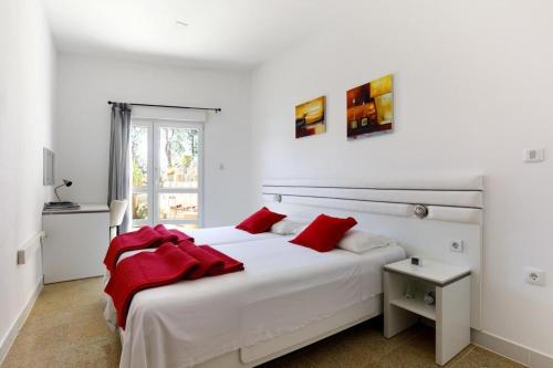 a white bedroom with a large white bed with red pillows at Ark Beach Apartments next to the beach in Stobrec in Split