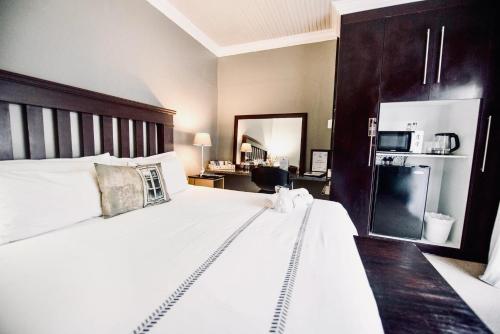 a bedroom with a large white bed and a kitchen at Cottonwood Guesthouse Oasis in Bloemfontein
