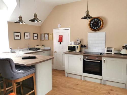 una cocina con armarios blancos y un reloj en la pared en The Courtyard Apartment at Cefn Tilla Court, Usk en Usk