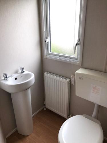 uma casa de banho com um lavatório, um WC e uma janela. em Caledonia Summertime em Jaywick Sands