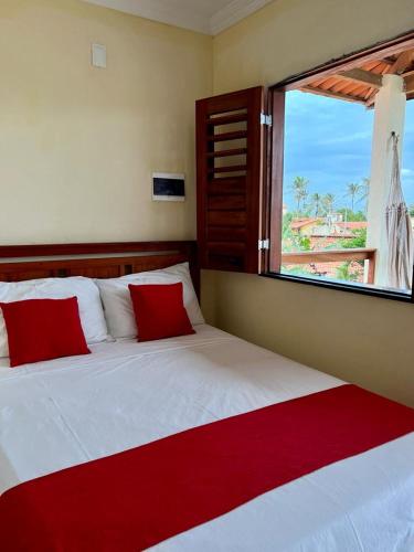 ein Schlafzimmer mit einem Bett mit roten Kissen und einem Fenster in der Unterkunft Suíte das flores em Guajiru in Trairi