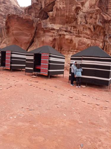 3 personnes debout sous des tentes noires et blanches dans le désert dans l'établissement Moon city camp, à Wadi Rum