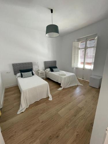 a white room with two beds and a window at HOSTAL LA CRUZ 1872 in Chipiona