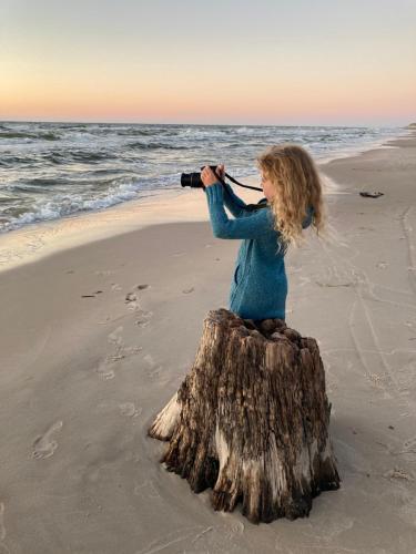 a girl sitting on a tree stump taking a picture of the ocean at Apartament z Jaskółką piętro- duży 90 m2 plus taras in Smołdzino