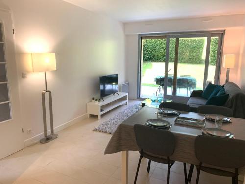 ein Wohnzimmer mit einem Tisch, Stühlen und einem Sofa in der Unterkunft Rez-de-jardin - Résidence avec Piscine - Deauville in Deauville