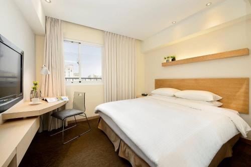 a bedroom with a bed and a desk and a television at Beacon Hotel in Taichung