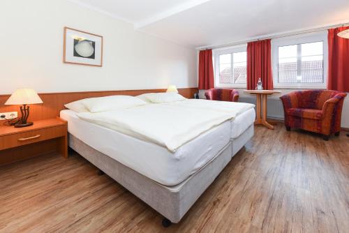 a bedroom with a large white bed and red curtains at Hotel Garni Benser Watt in Bensersiel