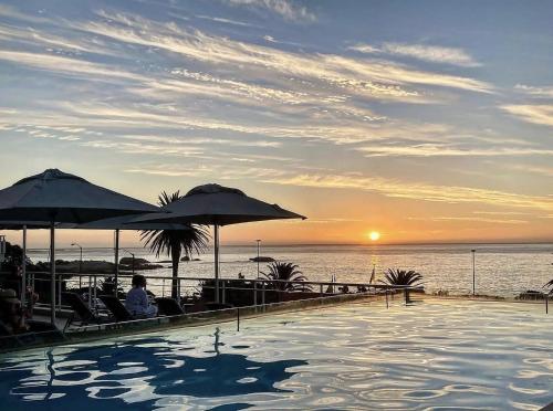 a swimming pool with a view of the ocean at sunset at South Beach Camps Bay Boutique Hotel in Cape Town