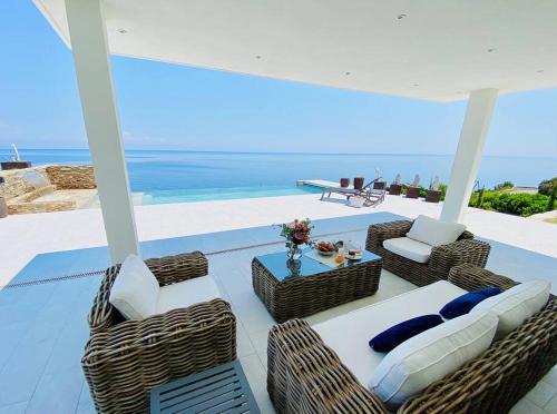 un patio con sillas y mesas de mimbre y el océano en Villa prestige au bord de l'eau- Pietracorbara, en Pietracorbara