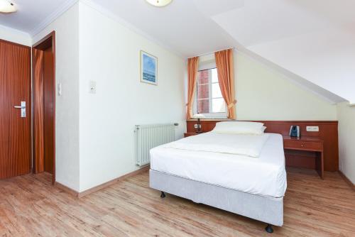 a white bedroom with a bed and a staircase at Hotel Garni Benser Watt in Bensersiel