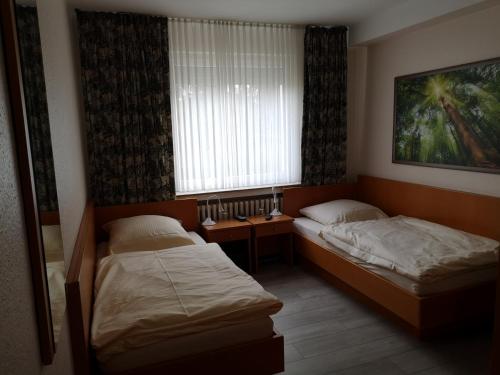 twee bedden in een kleine kamer met een raam bij Hotel Alscher in Leverkusen