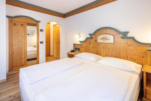a bedroom with a large white bed with a wooden headboard at Hotel Bellavista in Cavalese