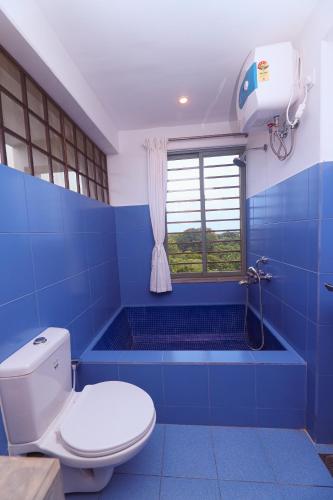 a blue bathroom with a toilet and a window at The Canopy Guest House in Auroville