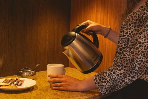 a woman holding a tea kettle on a table with a cup at San Juan Suites in Sucre