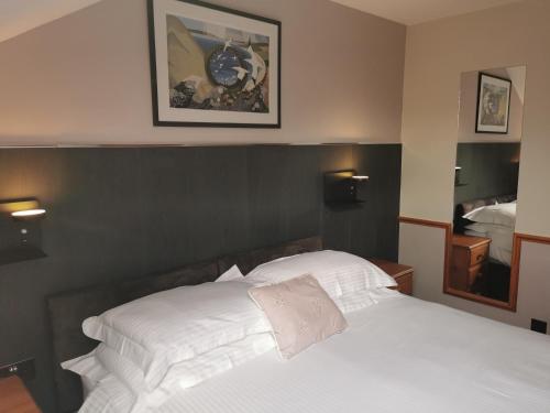 a bedroom with a white bed with a clock on the wall at Murray Arms Hotel and Seafood Restaurant, Orkney in Saint Margarets Hope