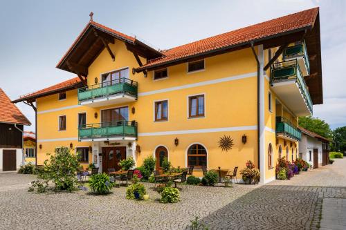 um edifício amarelo com varanda, mesas e bancos em Hotel Preishof em Kirchham