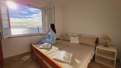 a woman sitting on a bed looking out a window at Blue Lagoon in Silba