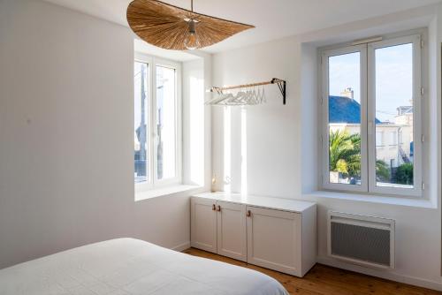 a white bedroom with a bed and two windows at Jolie maison proche centre-ville et plages in Granville