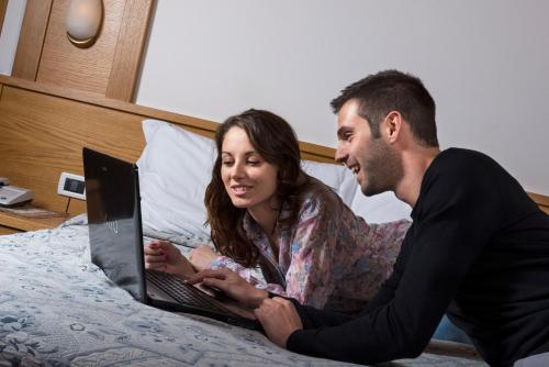 a man and woman sitting on a bed with a laptop at La Montanina Hotel in Val di Non in Malosco