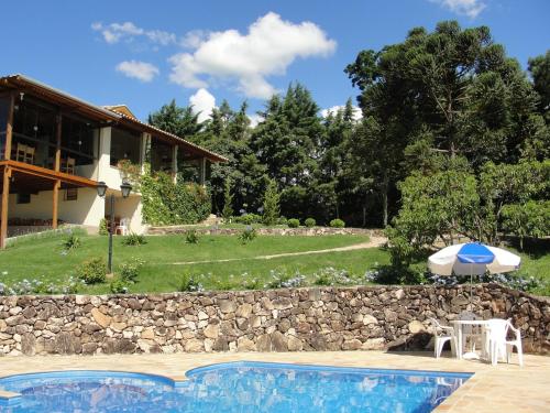 a swimming pool with an umbrella and a house at Pousada Morro Verde in Águas de Lindóia