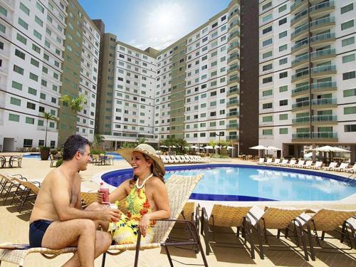 a man and woman sitting in chairs next to a swimming pool at Riviera Park Caldas Novas in Caldas Novas