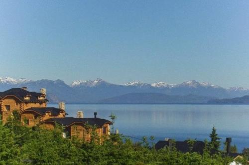 a house on the shore of a lake with snow covered mountains at Cabañas Chesa Engadina in San Carlos de Bariloche