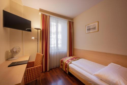 a hotel room with a bed and a desk and a window at Hotel De la Paix in Luzern