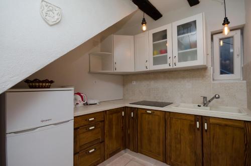 eine Küche mit Holzschränken und einem weißen Kühlschrank in der Unterkunft Under Ancient Roofs Vrbnik in Vrbnik