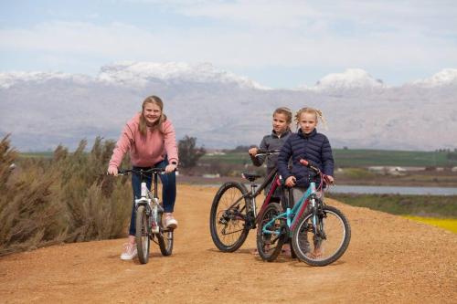 a woman and two children riding bikes on a dirt road at Rooikraal Farm Rondawel in Prince Alfreds Hamlet
