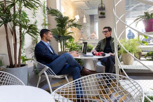 dois homens sentados numa mesa numa sala com plantas em Hôtel Marais Hôme em Paris