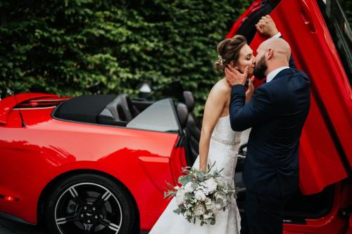 a bride and groom standing next to a red car at Magnus Resort in Szczyrk