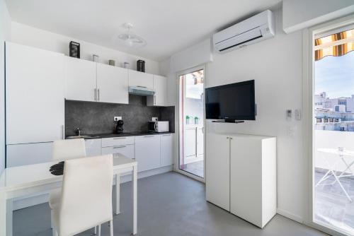 une cuisine avec des placards blancs, une table et une télévision dans l'établissement Appartement situé à 1 min de La Croisette, à Cannes