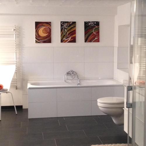 a bathroom with a tub and a toilet and some paintings at Ruhige 1 Zimmerwohnung Souterrain in Bortfeld