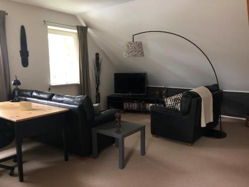 ein Wohnzimmer mit einem schwarzen Ledersofa und einem Tisch in der Unterkunft Gemütliche 1 12-Zimmer Wohnung in Hoisdorf