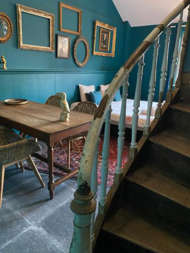 a dining room with blue walls and a table and stairs at Maison Jules in Sainte-Ode